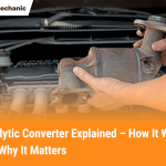 A mechanic holding a catalytic converter in front of a car engine, showing what a catalytic converter looks like and how it connects to a vehicle’s exhaust system.